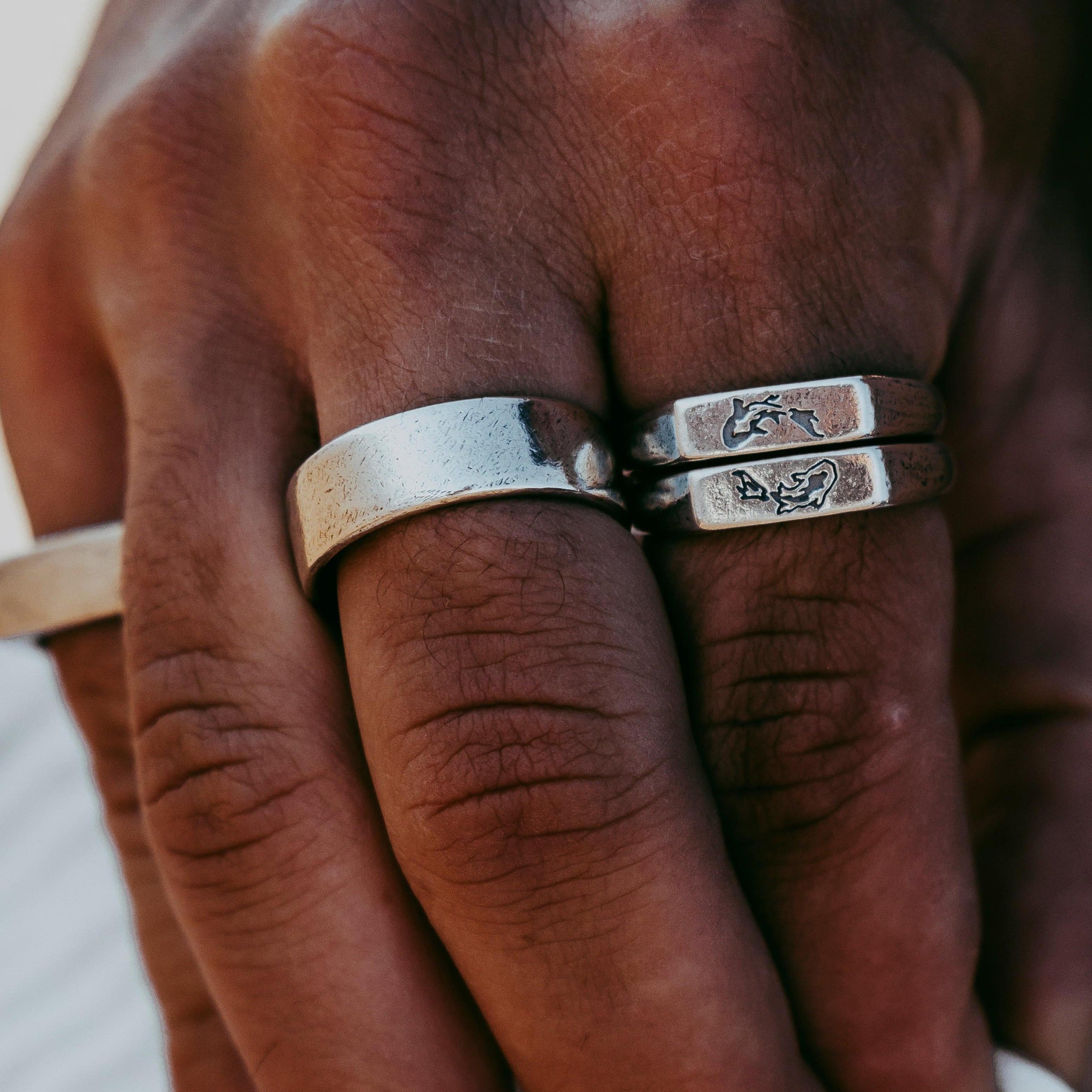 A close-up of a hand wearing three silver billie jo rings, two of which have engraved designs. The skin tone is medium, and the background is softly blurred. v1