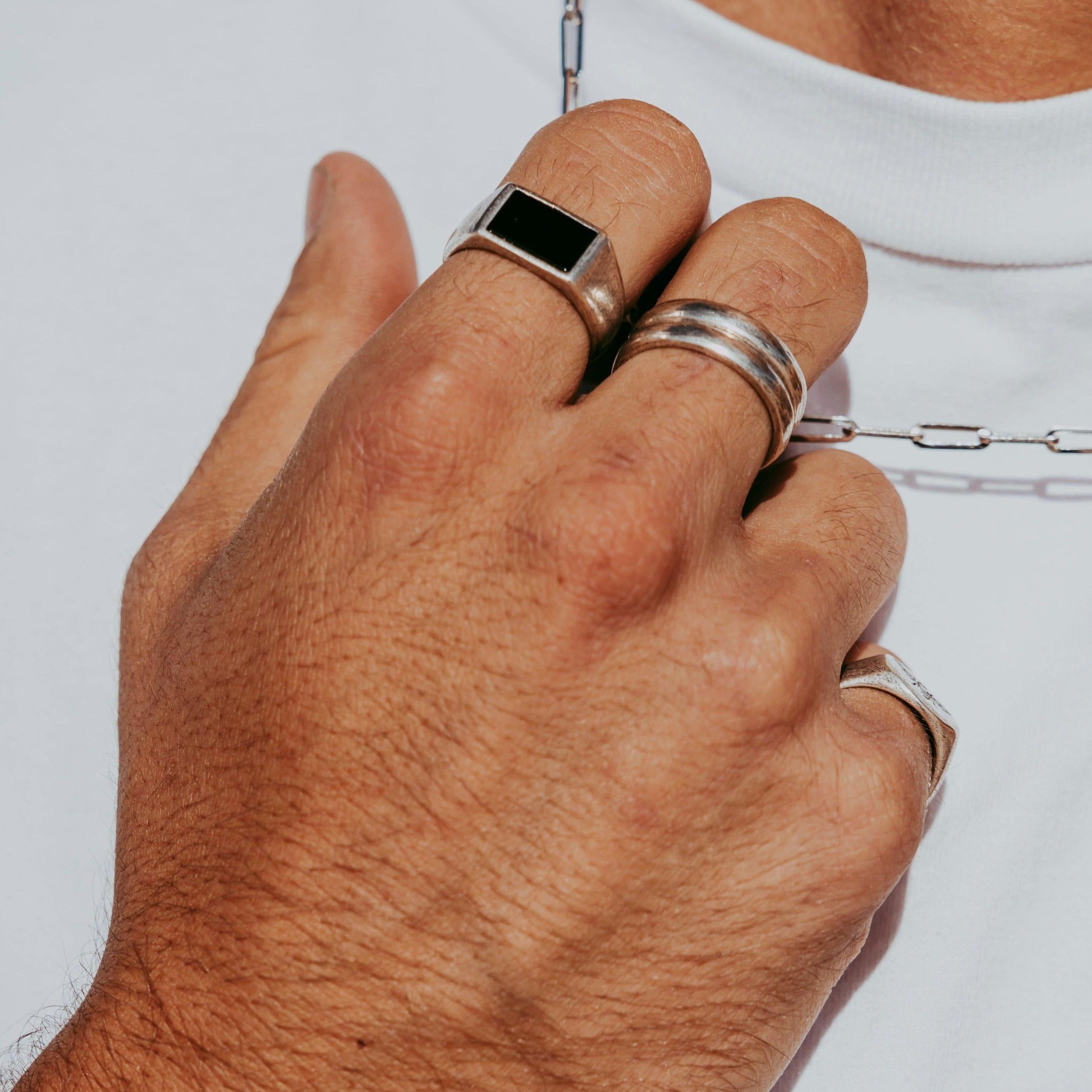 A close-up of a persons hand wearing several silver rings and holding a silver chain necklace, with the person dressed in a white shirt.