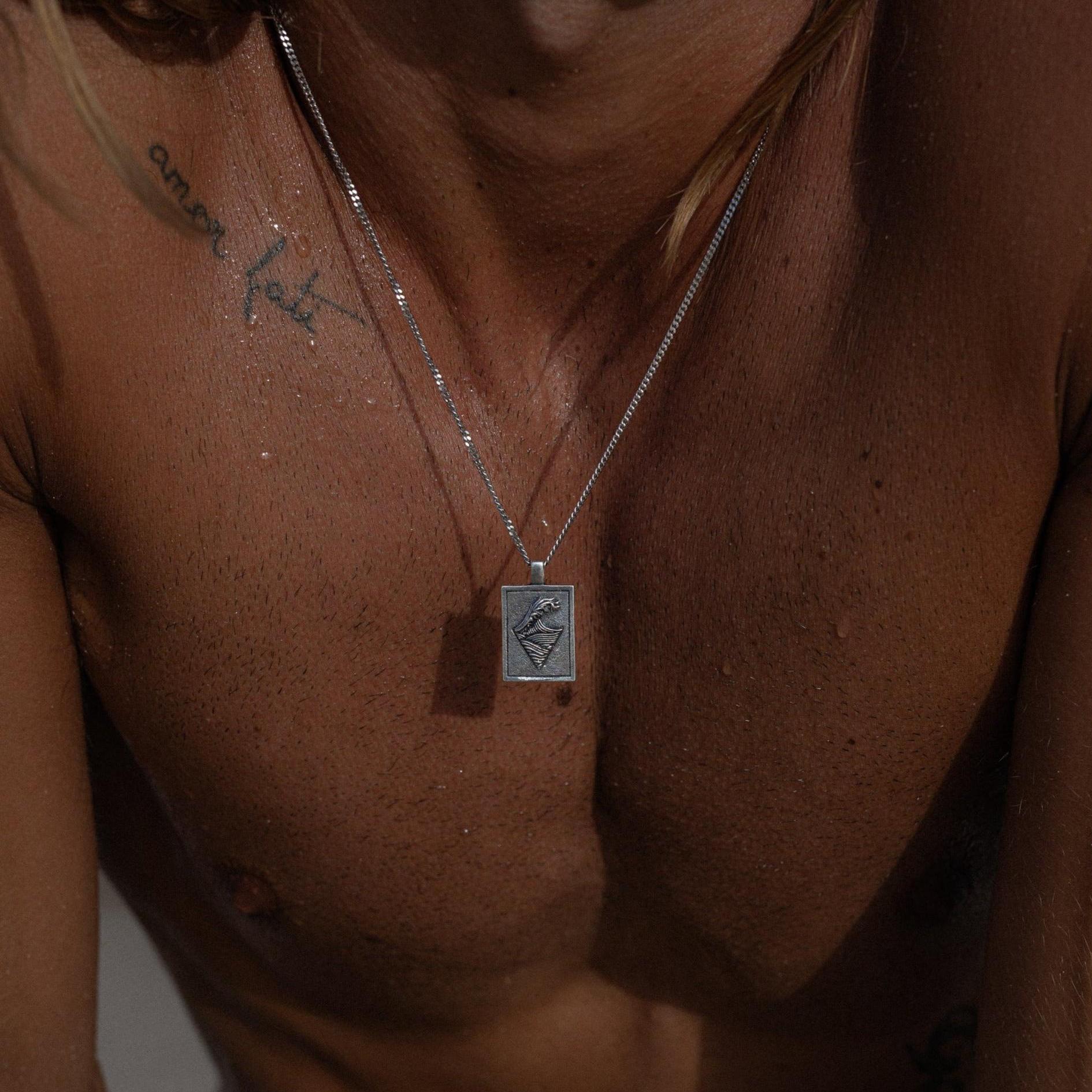 A close-up image showcasing a silver necklace with a square pendant that features an intricate design. The focus is on the jewelry, highlighting its craftsmanship and elegance. The necklace complements the silver rings worn on the person's fingers, known as 'Billie Jo rings,' which are prominently displayed and serve as the centerpiece of the image.
