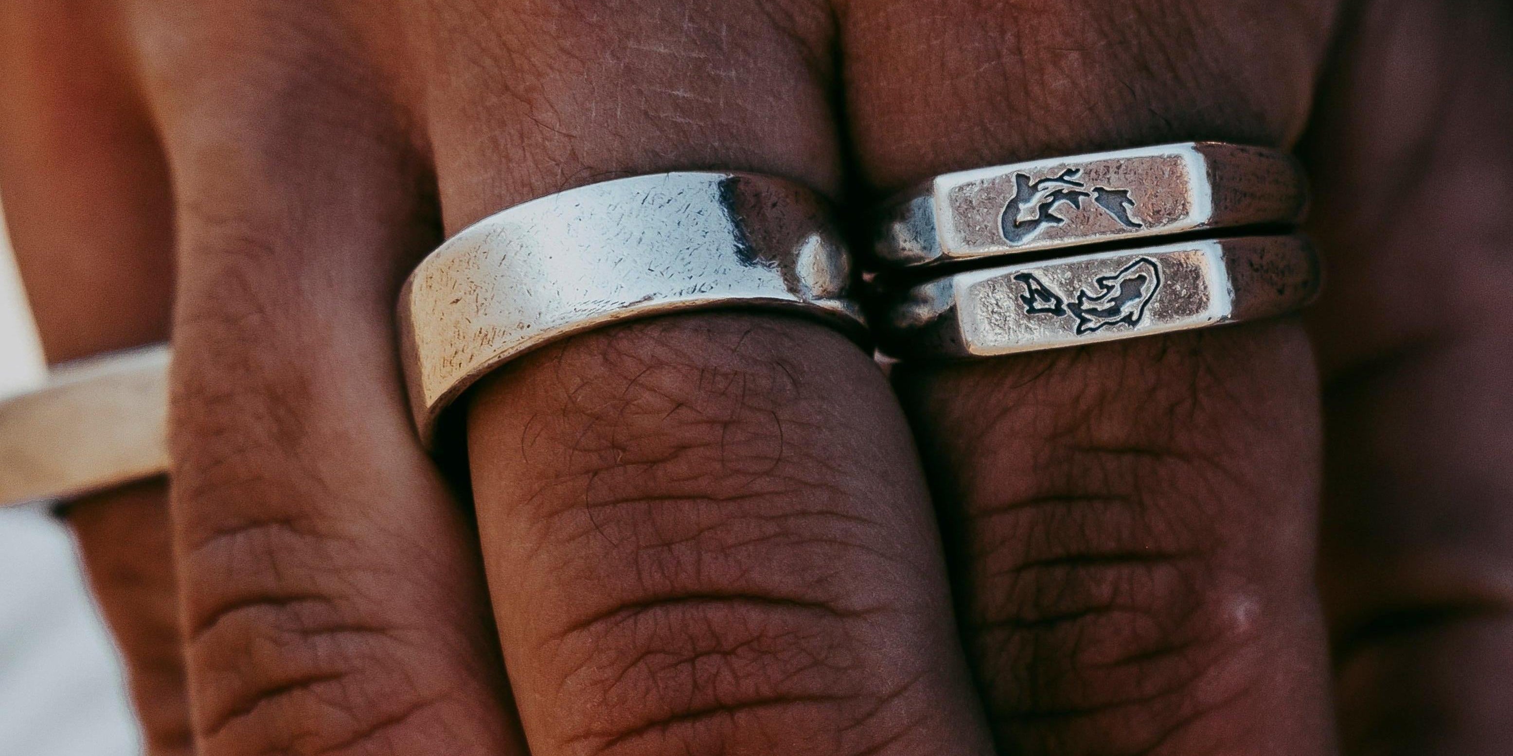 A close-up of a hand wearing three silver billie jo rings, two of which have engraved designs. The skin tone is medium, and the background is softly blurred. v1