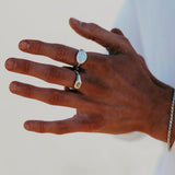 A close-up of a hand wearing two silver rings and a thin silver bracelet, with fingers slightly spread and a soft, neutral background.