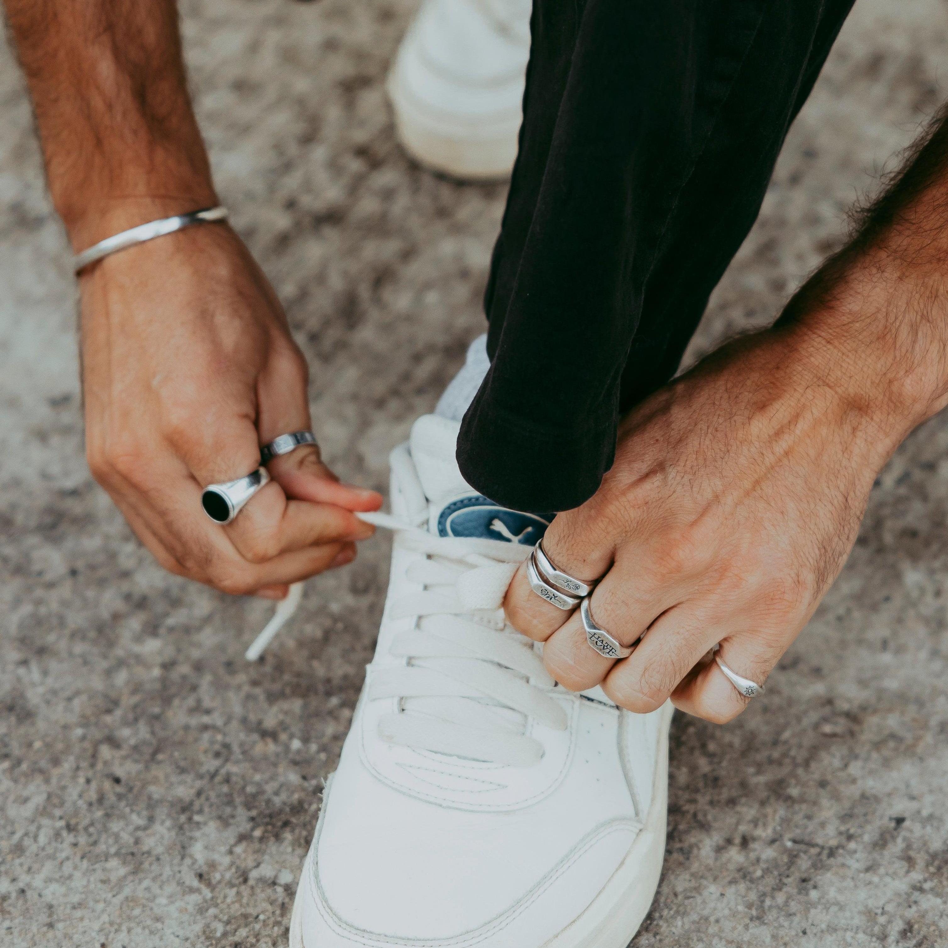 Man tying shoelaces while wearing the Abyss Ring with black onyx stone and multiple silver rings, casual street style