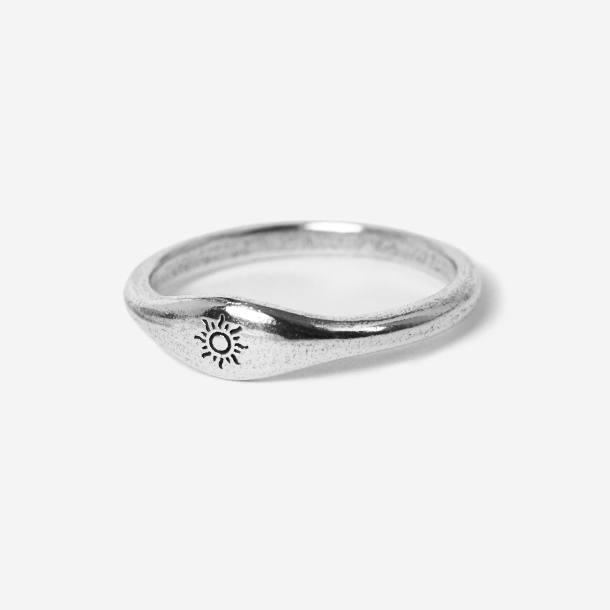 A simple silver ring with a slightly wavy band, featuring a small engraved sun design on one side, shown against a plain white background.