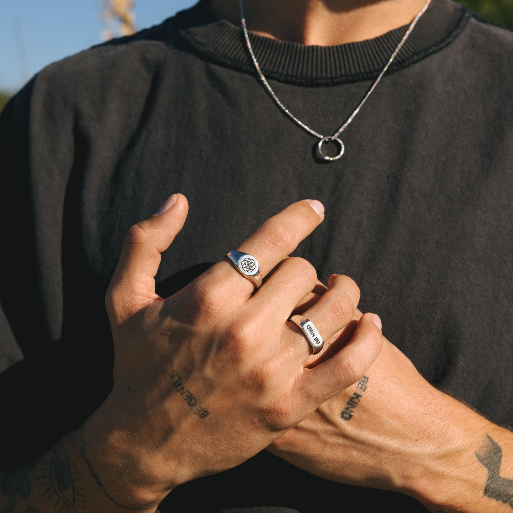 Person wearing a black shirt with visible tattoos on their arms, holding their hands together.