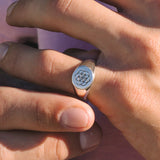 Close-up of a hand wearing a ring with a symbol on a pink background