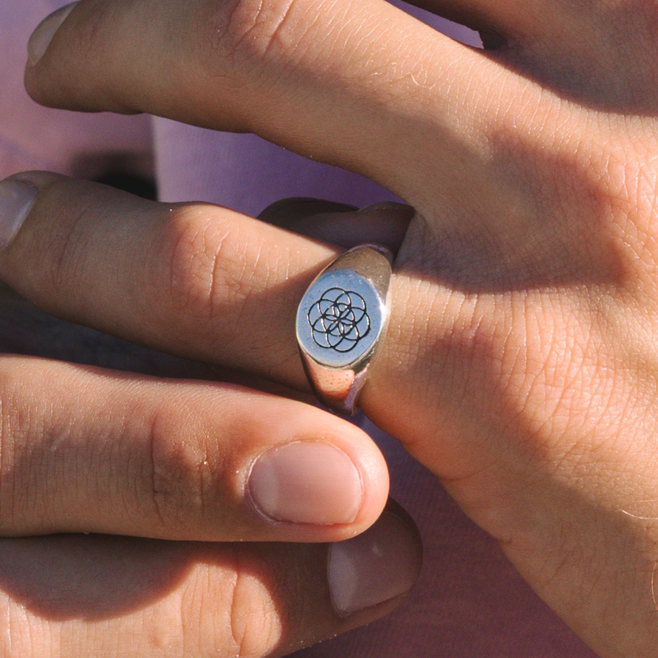 Close-up of a hand wearing a ring with a symbol on a pink background