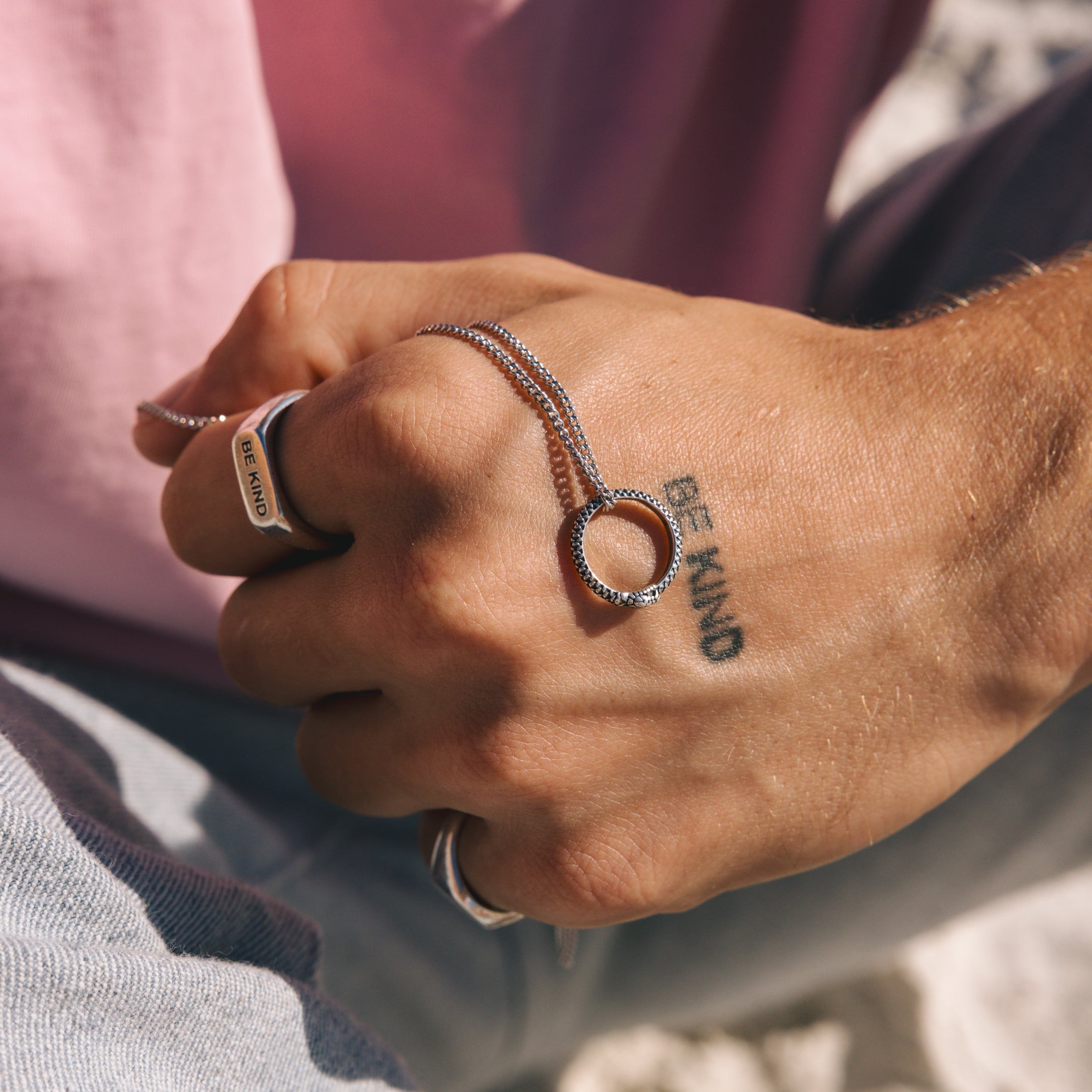 Hand wearing multiple rings with visible tattoos, set against a blurred natural background